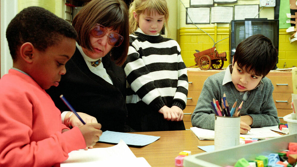 Teacher and three primary school children looking at a piece of work in a bright classroom
